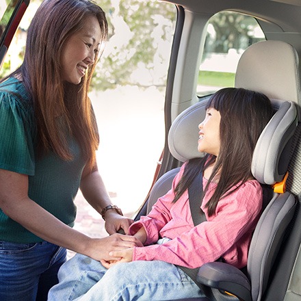 A mother buckling her daughter into her car seat