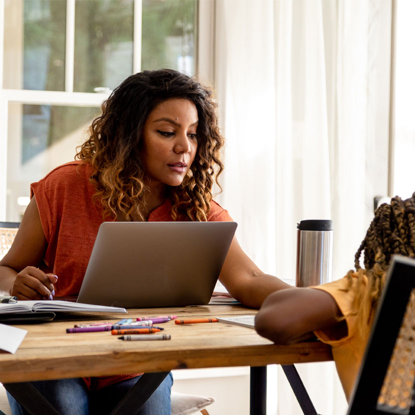 Woman at a laptop helping a child across the table